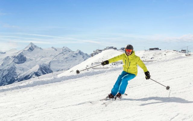 Schifahrer in einem blau grünen Schianzug fährt auf der Piste Schi