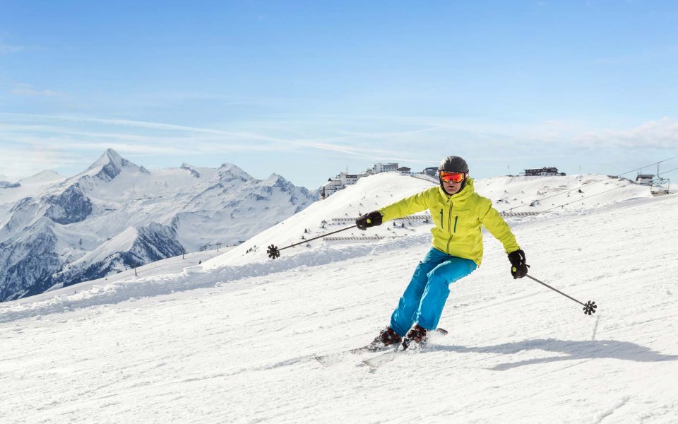 Schifahrer in einem blau grünen Schianzug fährt auf der Piste Schi