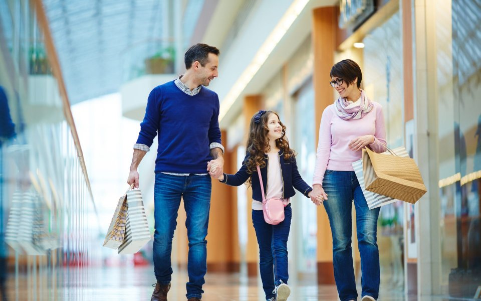 Vater und Mutter halten ihr Kind an den Händen und tragen Papiertaschen in den Händen